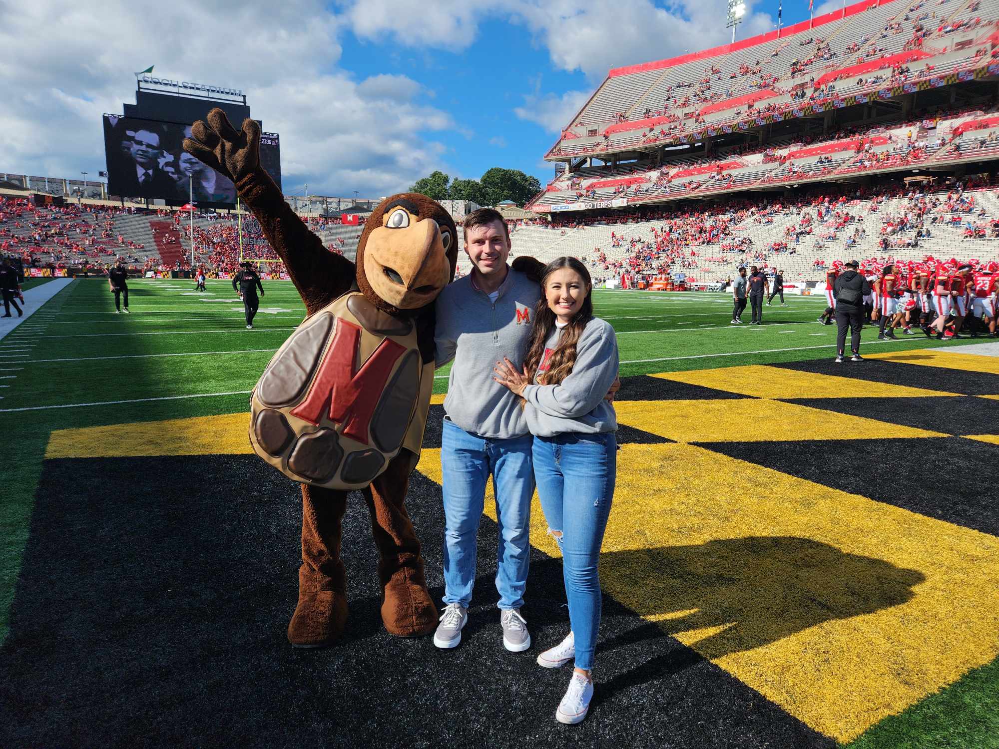 Testudo (left) posed with Collin Vincent (middle) and Hallie Pennington (right) on the field of SECU Stadium after the couple's engagement. Image courtesy of Collin Vincent.