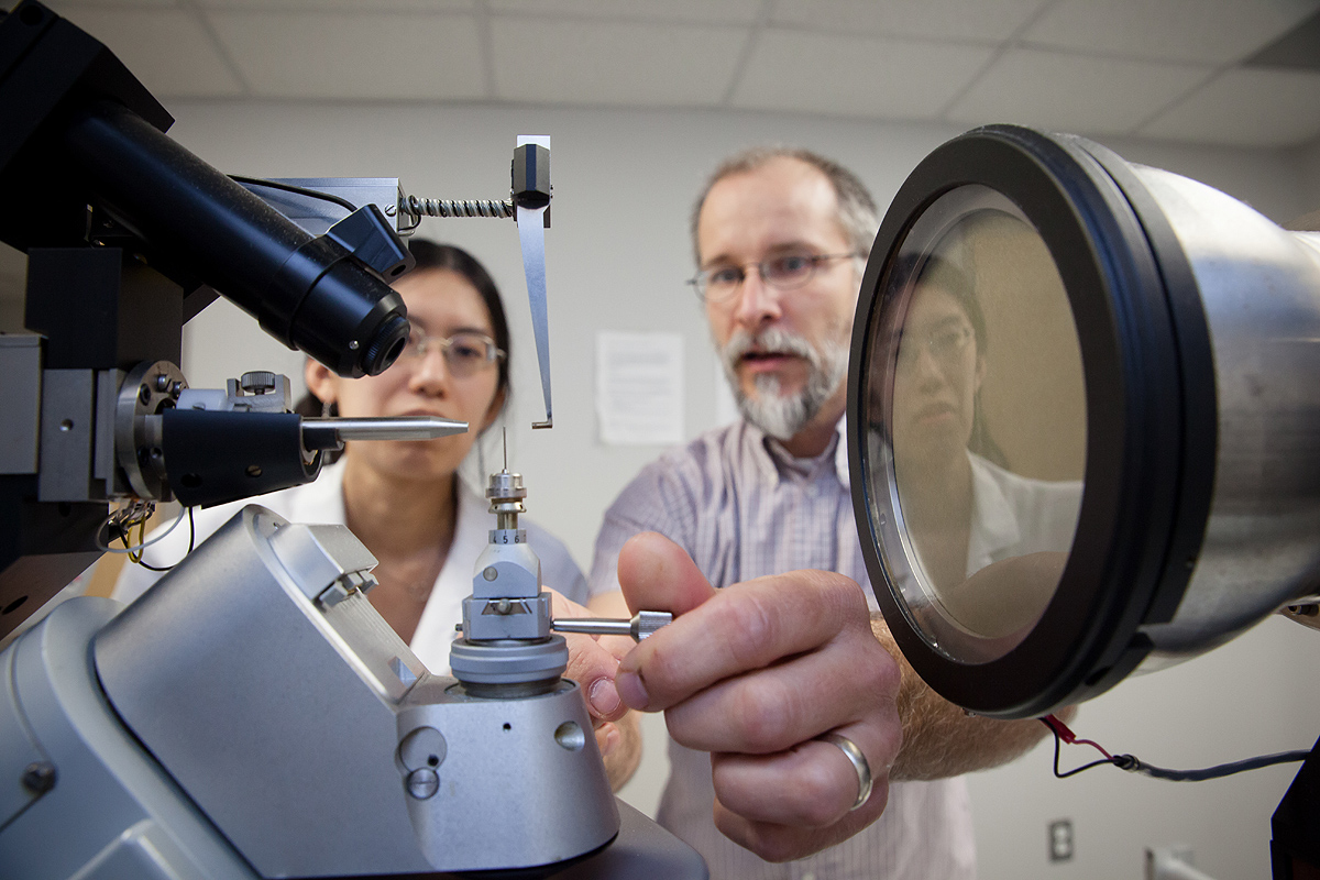 A female graduate student and a male professor adjusting a pice of equipment.