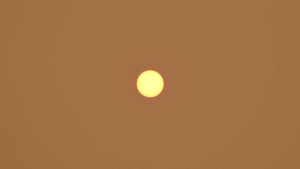 The sun appearing as a small yellow circle in the center of the image against a burnt orange sky.