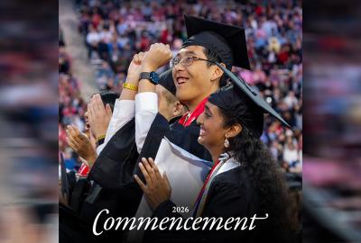 Two students in graduation regalia celebrating, with a blurred crowd in the background.
