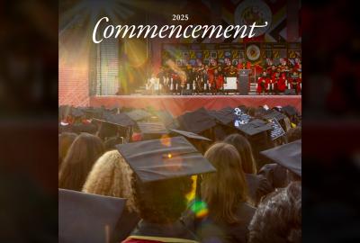 Photo of a large crowd of people at commencement. We see the students from the back, and ahead, a platform party facing the audience.