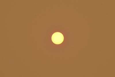 The sun appearing as a small yellow circle in the center of the image against a burnt orange sky.