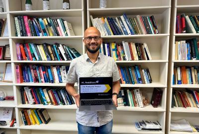 Pratyush Tiwary holding a laptop standing in front of several bookshelves