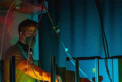 Colenso Speer using microscopy equipment that is lit up in a dark room