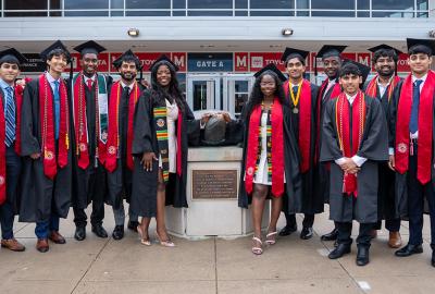 A group of graduates in regalia standing with a bronze Testudo statue. Credit: Mark Sherwood.