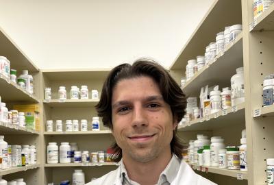 Isaac Robinson in a white lab coat in front of shelves of medications at Giant Pharmacy.