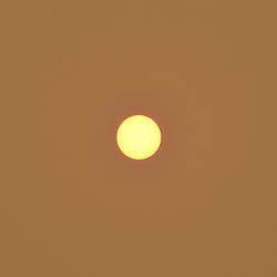 The sun appearing as a small yellow circle in the center of the image against a burnt orange sky.