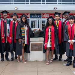 A group of graduates in regalia standing with a bronze Testudo statue. Credit: Mark Sherwood.